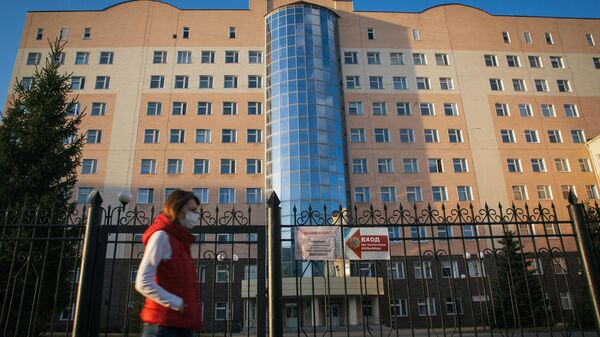 Девушка в защитной маске проходит мимо закрытого входа на территорию республиканской клинической больницы в Уфе