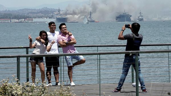 Люди фотографируются на фоне горящего универсального десантного корабля USS Bonhomme Richard (LHD 6) Люди фотографируются на фоне горящего универсального десантного корабля USS Bonhomme Richard (LHD 6)