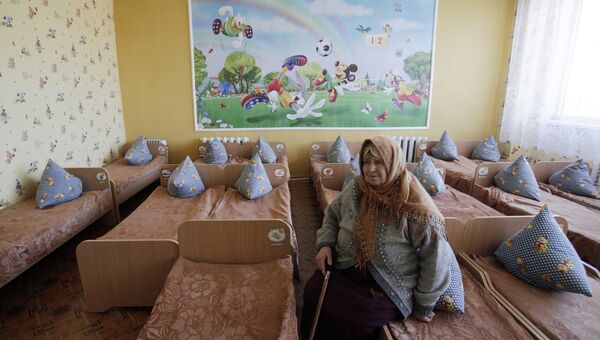 Пожилая женщина сидит на кровати в детском саду. Архивное фото Пожилая женщина сидит на кровати в детском саду. Архивное фото