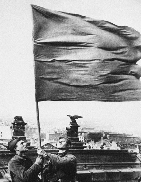 Два бойца держат развевающееся знамя стоя на крыше рейхстага Два бойца держат развевающееся знамя стоя на крыше рейхстага