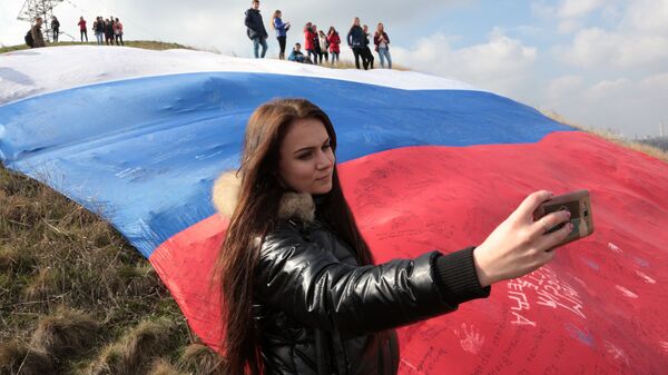Девушка делает селфи на фоне огромного флага России на фестивале Крымская весна в селе Мирное Симферопольского района Республики Крым Девушка делает селфи на фоне огромного флага России на фестивале Крымская весна в селе Мирное Симферопольского района Республики Крым