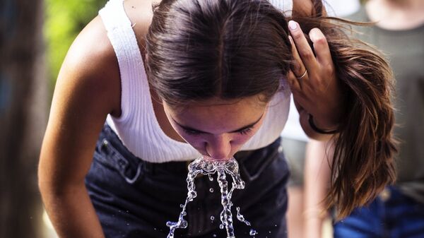 Девушка пьет воду из уличного питьевого фонтанчика