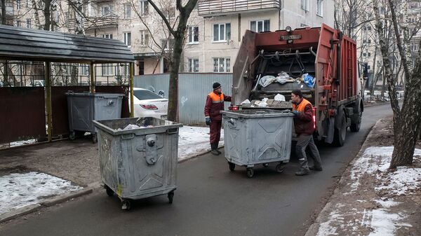 Сотрудники коммунальных служб выгружают мусор из контейнеров в мусоровоз Сотрудники коммунальных служб выгружают мусор из контейнеров в мусоровоз